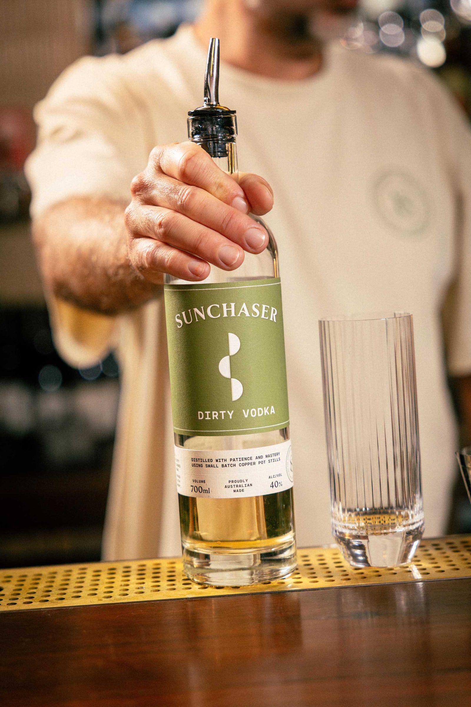 A bartender presenting a bottle of Sunchaser Dirty Vodka across the bar.