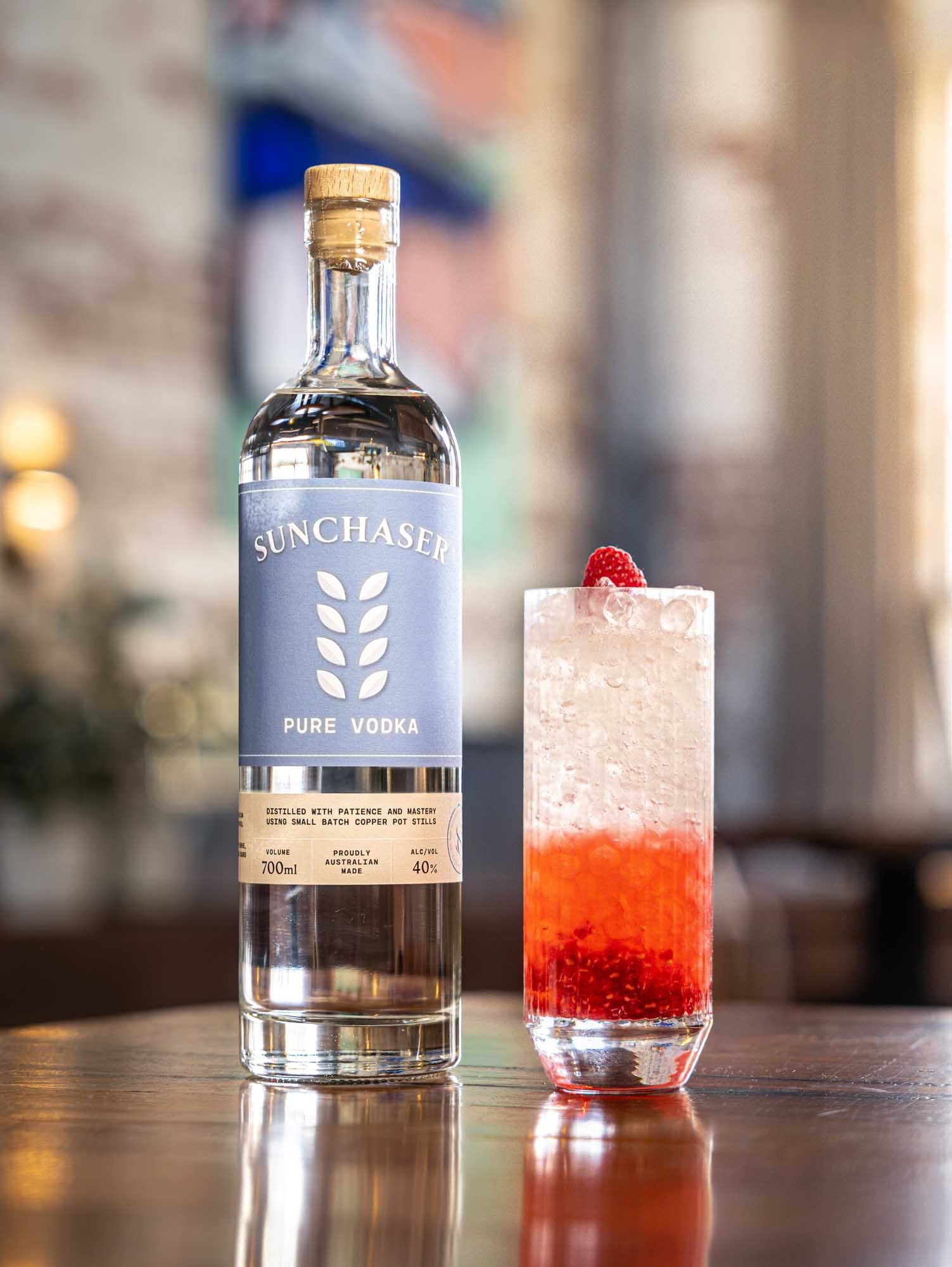 A Spring Punch with a raspberry-red base beside a bottle of Sunchaser Pure Vodka.